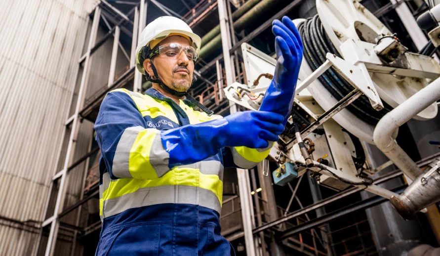 Een industriële reiniger van Buchen Industrial Services inspecteert zijn zuurbestendige handschoenen