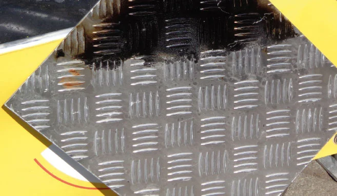 Een metalen antislip vloerplaat waarvan de helft gereinigd werd door Buchen Industrial Services en de andere helft niet om het goede resultaat van de reiniging aan te tonen