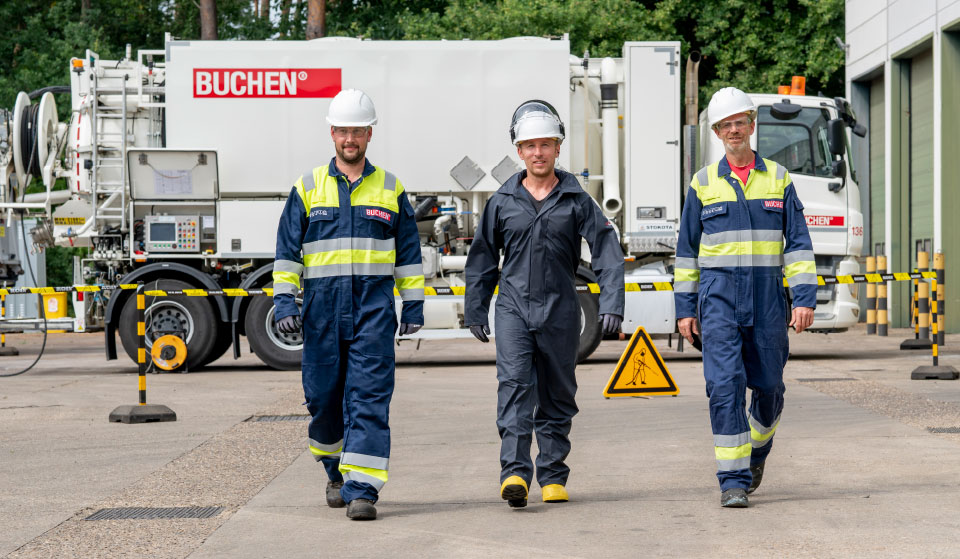Collega's van Buchen Industrial Services wandelen weg van een industriële reinigersvrachtwagen terwijl ze persoonlijke beschermingsmiddelen dragen
