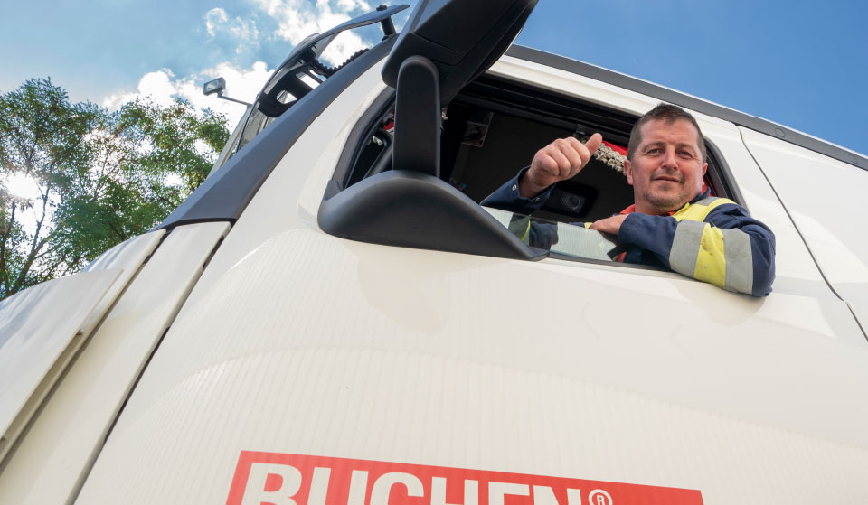 Vrachtwagenchauffeur van Buchen Industrial Services hangt uit het raam van een vrachtwagen en steekt zijn duim omhoog terwijl hij glimlacht